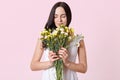 Slender beautiful brunette woman holding yellow pink bouquet, closing her eyes, feeling smell of spring flowers, wearing white