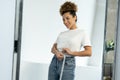 Slender black woman standing in front of a mirror measures her waist with a measuring tape after losing weight Royalty Free Stock Photo