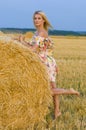 Vertical portrait of a beautiful slender blonde near a haystack on a background of sky and field