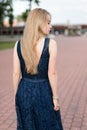 Slender blonde girl in dark-blue dress turned her back looking away on pavement Royalty Free Stock Photo