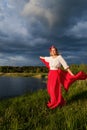 A slender caucasian girl in red skirt and white blouse with a red shawl in her hands against the background of a stormy sky Royalty Free Stock Photo