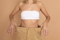 Slender Caucasian lady in white bra underwear and large oversize pants showing slim waist on skin colored background