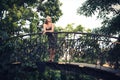 A slender elegant girl in a dark dress with blond hair stands in a park alley on a bridge Royalty Free Stock Photo