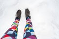 Slender female legs in bright multicolored leggings and warm suede lace-up boots stand on a cleared path, next to a