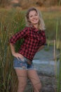 A slender girl with blond hair stands in the reeds on the riverbank and laughs Royalty Free Stock Photo