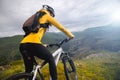 A slender girl cyclist with red hair in a helmet and with a backpack stands on a mountain bike high in the mountains Royalty Free Stock Photo