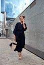 Slender girl in a long black dress walks down the street talking on the phone Royalty Free Stock Photo