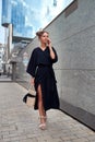 Slender girl in a long black dress walks down the street talking on the phone Royalty Free Stock Photo