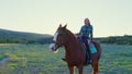 Girl sits astride horse who walks through meadow