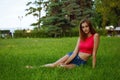 Slender girl sits in green grass in a lush garden