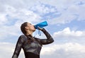 Slender girl in sports clothes drinking water from a bottle against the sky with clouds ,the athlete