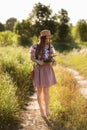 A slender girl in a straw hat and with a straw handbag holding a bouquet of daisies in the meadow. Summer sunset, the concept of