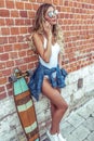 Slender girl in summer city background of wall calls phone skateboard longboard. Fashionable stylish woman bathing suit Royalty Free Stock Photo
