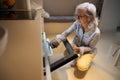 Slender gray-haired pensioner takes out hot baking sheet from oven