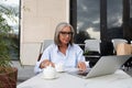 a slender gray-haired woman of mature years dressed in a light blue shirt spends a lunch break sitting on the terrace