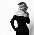 Slender lady with curly blonde hair in stylish black dress standing with her back to us, turning her head to the side Royalty Free Stock Photo