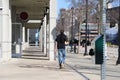 A slender man in a black shirt and jeans walking along the sidewalk in the city surrounded by office buildings, skyscrapers