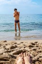 A slender man wipes his wet face with his hands when he comes out of the sea on the beach. Blurry female feet soiled in the sand Royalty Free Stock Photo