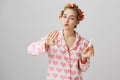 Slender ordinary caucasian girl in cozy outfit, wearing red hair curlers and blowing at fingers while painting nails Royalty Free Stock Photo