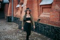 A slender smiling young girl with blond long hair, in black leggings, a tank top, a beige jacket and a hat Royalty Free Stock Photo