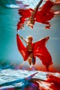 girl with an athletic figure and blond hair, with red material and light underwear, in a ballet pose underwater Royalty Free Stock Photo