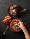 Slender woman hand pouring grated cheese on pumpkin stuffed with rice, mushrooms and onions and smaller pumpkins with red rice and Royalty Free Stock Photo