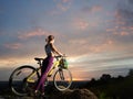 Slender woman with mountain bike is standing on hill under beautiful sky at sunset Royalty Free Stock Photo