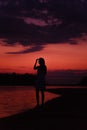 A slender woman is standing on the beach. A beautiful young happy woman admires the sunset and raises her hand to her Royalty Free Stock Photo