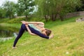 Slender young brunette yogi performs challenging yoga exercises on the green grass in the summer against the backdrop of nature Royalty Free Stock Photo