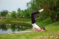 Slender young brunette yogi performs challenging yoga exercises on the green grass in the summer against the backdrop of nature Royalty Free Stock Photo