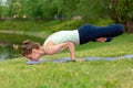 Slender young brunette yogi performs challenging yoga exercises on the green grass in the summer against the backdrop of nature Royalty Free Stock Photo