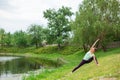 Slender young brunette yogi performs challenging yoga exercises on the green grass in the summer against the backdrop of nature Royalty Free Stock Photo