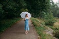 A slender young girl with blond long hair, in a blue summer dress and shoes, walking with a white umbrella Royalty Free Stock Photo