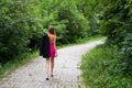 A slender young girl with long blond hair, in a short stylish pink dress, walks beautifully along the path Royalty Free Stock Photo