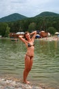 Slender young girl stands in a bathing suit on the banks of the river on a background of mountains Royalty Free Stock Photo