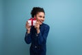 a slender young hispanic brunette woman with fluffy curly hair in a blue denim suit hugging a gift box in her hands Royalty Free Stock Photo