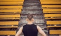 A slender young man in black sportswear stands in front of the stairs stadium stands. ready for action, step to victory, challenge