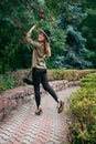 A slender young smiling girl with blond long hair, in black leggings, a tank top, a beige jacket and a hat Royalty Free Stock Photo