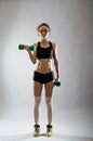A slender young woman with a dumbbell on a gray background.