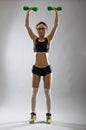 A slender young woman with a dumbbell on a gray background.