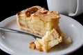 A slice of apple pie with pie on fork on white ceramic plate next to a fork. Black background. Royalty Free Stock Photo