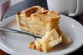 A slice of apple pie with pie on fork on white ceramic plate next to a fork. Black and brown table. Royalty Free Stock Photo