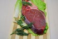 Slice of beef with bone and herbs on a wooden board.