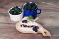 Slice of berry pie on cutting board, fresh berries of blackberries, blueberries, mint leaves, in white bowl and blue mug on wooden Royalty Free Stock Photo