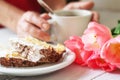 Slice of biscuit tiramisu cake, pink tulips and female hands with cup of coffee Royalty Free Stock Photo