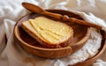 Slice of bread with ghee on a wooden plate, accompanied by a wooden spoon, against a soft white fabric. Royalty Free Stock Photo