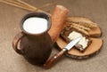 A slice of buttered bread on a wooden board, a crock of milk and mature ears