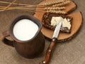 A slice of buttered bread on a wooden board, a crock of milk and mature ears