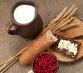 A slice of buttered bread on a wooden board, a crock of milk, a metal cup of red currants and mature ears Royalty Free Stock Photo