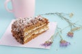 Slice of cake with icing on duck egg blue background with dried flowers and pink cup of milk